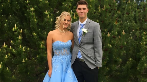 Una pareja en ropa formal está frente a árboles verdes en el terreno de la Bowness High School.