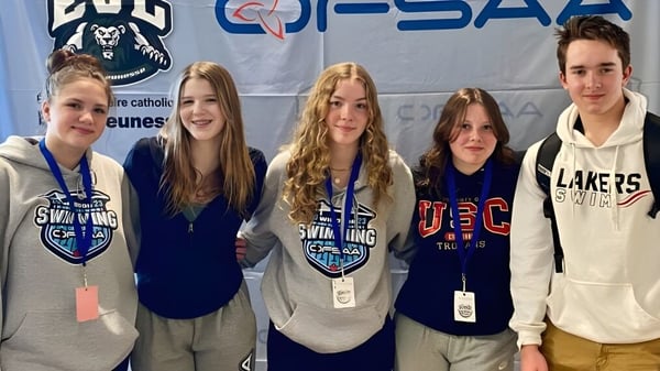 Un grupo de estudiantes de la Bracebridge and Muskoka Lakes Secondary School está frente a un banner con el logo de una organización deportiva.