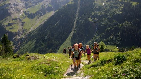 Un grupo de estudiantes del Bradfield College camina a través de un paisaje montañoso verde con un denso bosque de fondo.