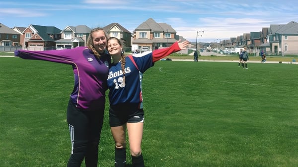 Dos estudiantes de la Bradford District High School se abrazan en un campo deportivo frente a casas coloridas.