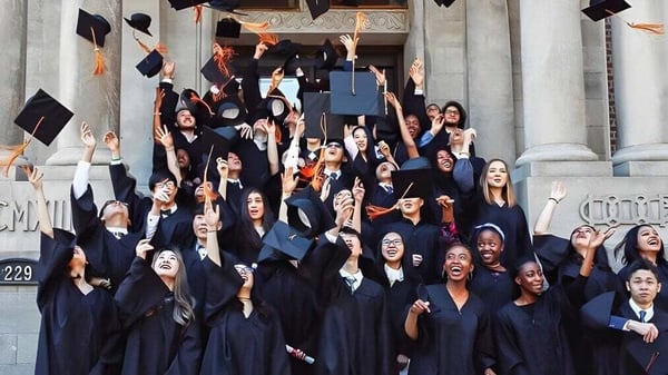 Un gran grupo de graduados del Braemar College en togas negras se reúne en las escaleras de un edificio majestuoso para celebrar su graduación.