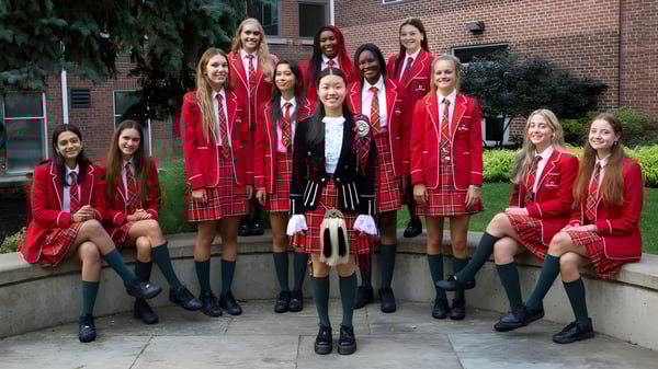 Un grupo de estudiantes en uniformes rojos está frente a un edificio de ladrillo en el campus de Branksome Hall.