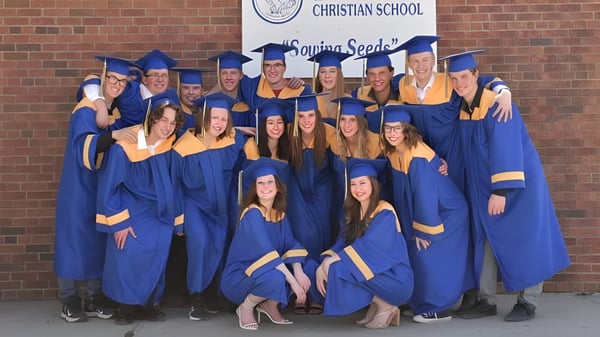 Un grupo de graduados de la Brant Christian School posa frente a un banner escolar.