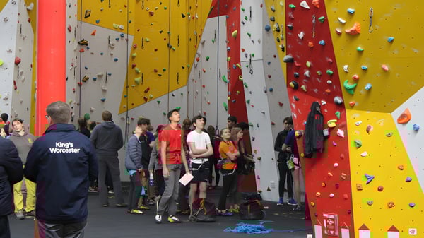 Estudiantes de la Bredon School están con equipo de escalada frente a una pared de escalada colorida en el gimnasio de escalada.