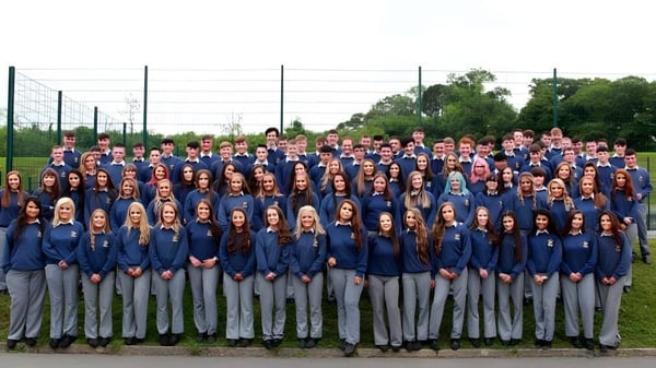 Un gran grupo de estudiantes del Breifne College está junto al aire libre frente a un fondo de árboles y líneas eléctricas.