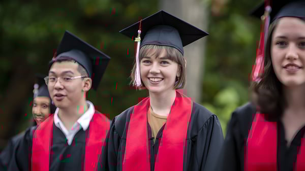 Un grupo de graduados está vestido con toga y birrete frente a un fondo natural en el campus de la Brentwood College School.