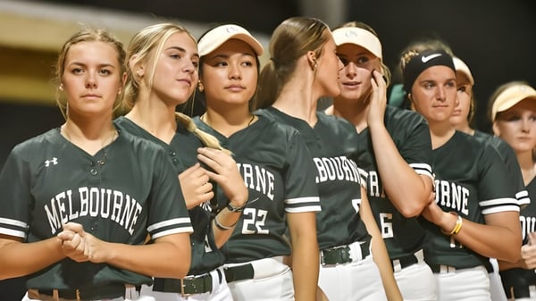 Un grupo de atletas femeninas en uniforme verde y blanco está en un campo de softball en Brevard County Public Schools.