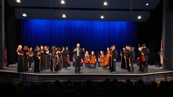 Una gran orquesta de la Brevard County Public Schools se presenta en un escenario con cortinas azules y focos.