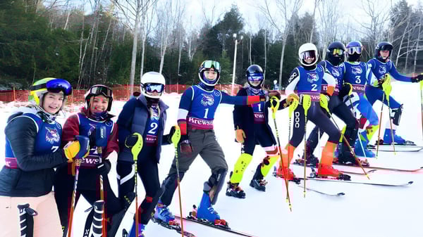 Un grupo de esquiadores con uniformes de colores está de pie en una pendiente cubierta de nieve en el terreno de la Brewster Academy.
