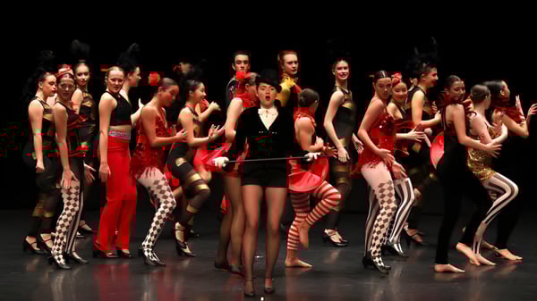 Estudiantes de Brighton College actúan en coloridos disfraces en un escenario oscuro.