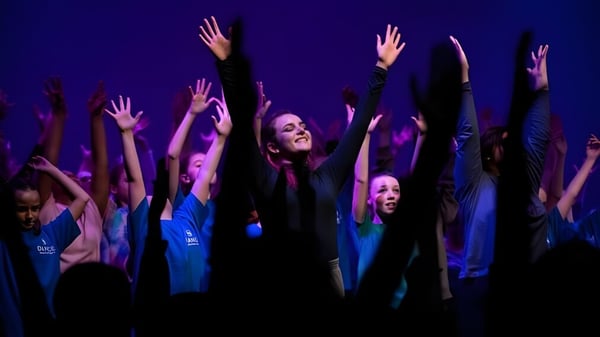 Un grupo de alumnas de Brighton Girls levantan los brazos en un gesto de júbilo frente a un fondo oscuro con iluminación violeta y azul.