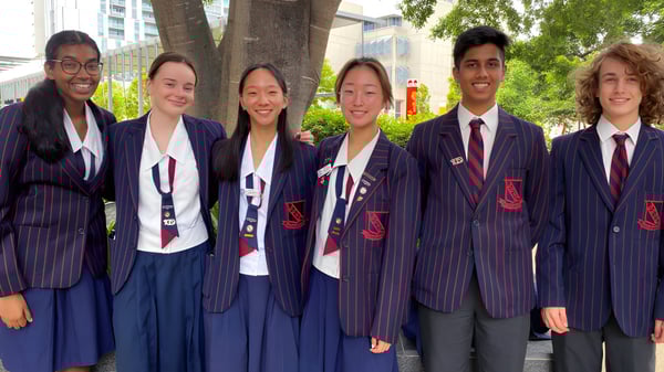 Un grupo de estudiantes de la Brisbane State High School se encuentra frente a un fondo urbano arbolado.