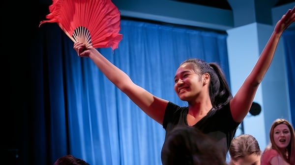 Una mujer en un vestido negro sostiene un abanico rojo y actúa en el escenario de la British International School Houston.