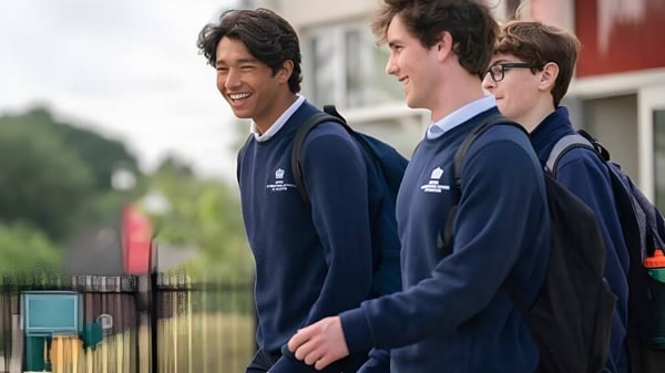 Tres estudiantes en uniformes azul marino están juntos en el área exterior de la British International School Houston y sonríen.