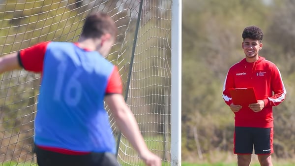 Dos futbolistas están en el campo del Brockenhurst College frente a la portería.