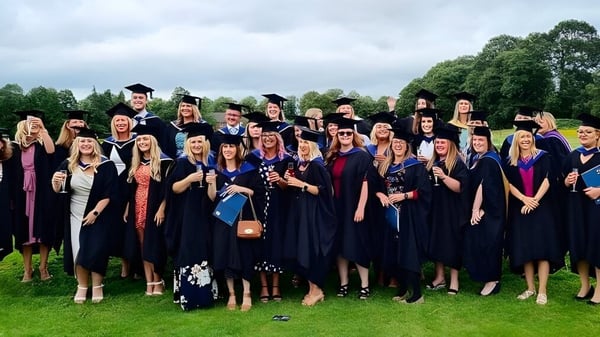 Un grupo de graduados está afuera en el área verde del campus del Brockenhurst College con vestimenta académica.