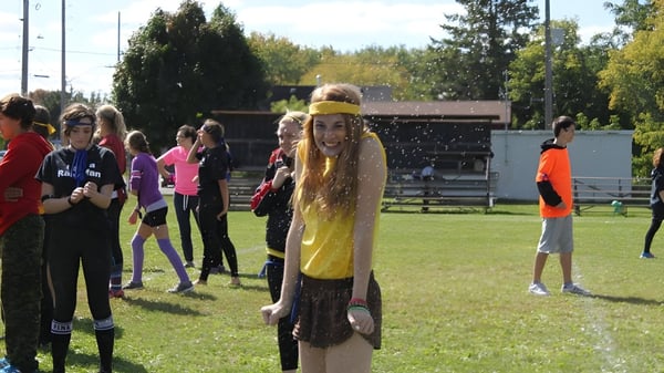 Un grupo de estudiantes en un prado con árboles alrededor frente a un edificio en el campus del Brockville Collegiate Institute.