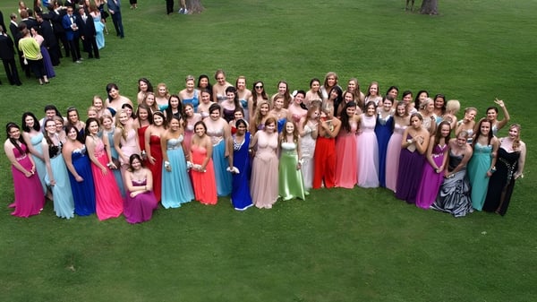 Un gran grupo de estudiantes del Brockville Collegiate Institute en vestidos coloridos está en un prado.