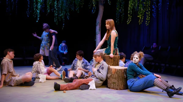 Un grupo de estudiantes y adultos del Brooke House College se reúnen alrededor de un tocón en un bosque sombrío.