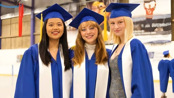 Tres estudiantes en togas de graduación azules celebran su éxito en la Brooks Secondary School.