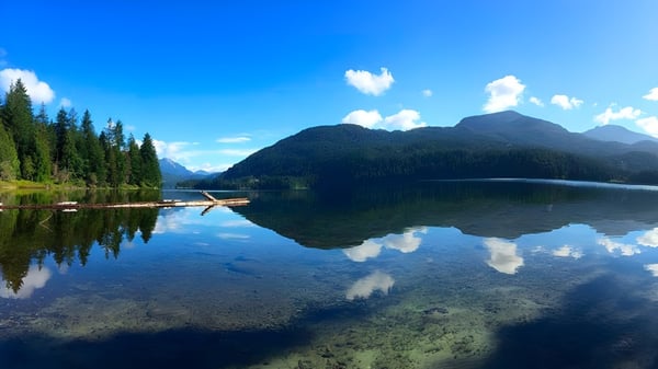 Un lago tranquilo con bosques y montañas refleja el paisaje en el terreno de la Brooks Secondary School.
