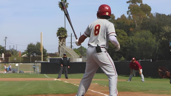 Un beisbolista de la Buena High School está en la camiseta blanca con el número 8 en el campo con palmeras de fondo.