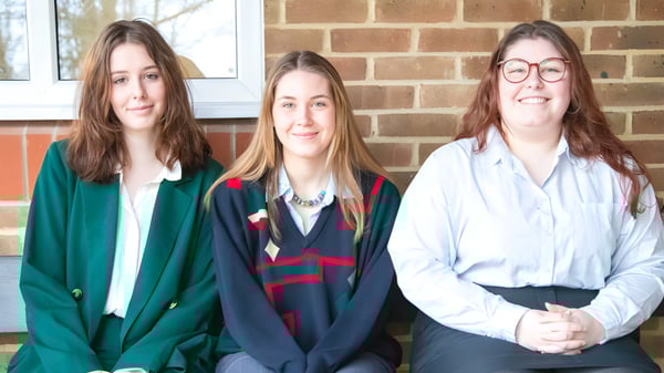 Tres alumnas de Burgess Hill Girls están de pie frente a una pared de ladrillo.