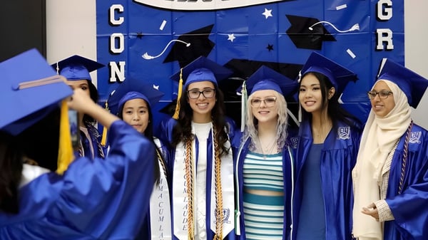 Alumnas de Burlington Central High School están en ropa de graduación frente a un fondo con el texto Congratulations.