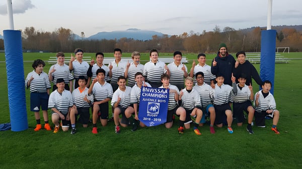 Un grupo de alumnas y alumnos de la Burnaby Mountain School está en el campo de fútbol con montañas al fondo.