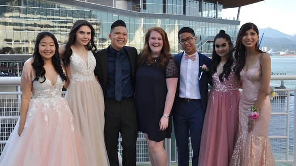 Un grupo de estudiantes en ropa formal está frente al moderno edificio de vidrio de la Burnaby South School.
