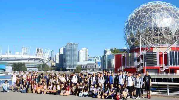 Un grupo de estudiantes se reúne frente al moderno edificio de cúpula de la Burnsview Secondary School ante el paisaje urbano.