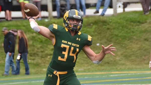Un jugador de fútbol americano de la Burr and Burton Academy en camiseta verde lanza un balón de fútbol en el campo.