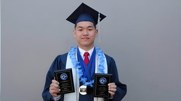 Un graduado de la Byrne Creek School está frente a un fondo gris y sostiene dos premios en las manos.