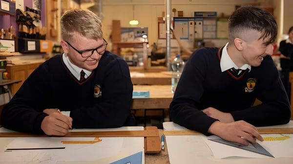 Dos estudiantes de la Cabinteely Community School están sentados juntos en una mesa y se concentran en su trabajo.