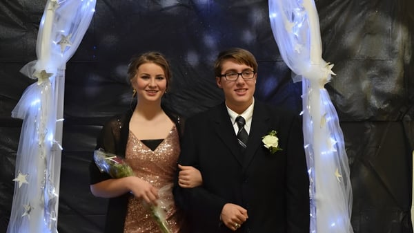 Una pareja vestida formalmente está bajo un arco decorativo en una celebración de boda en el terreno de la Cadillac Heritage Christian School.
