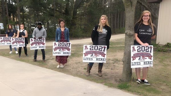 Un grupo de estudiantes de la Cadillac Heritage Christian School está con carteles en un sendero del bosque.