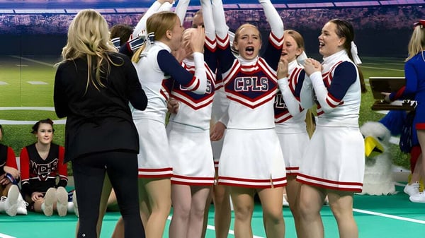 Las cheerleaders de la Cair Paravel Latin School celebran en el campo deportivo frente a una gran multitud.