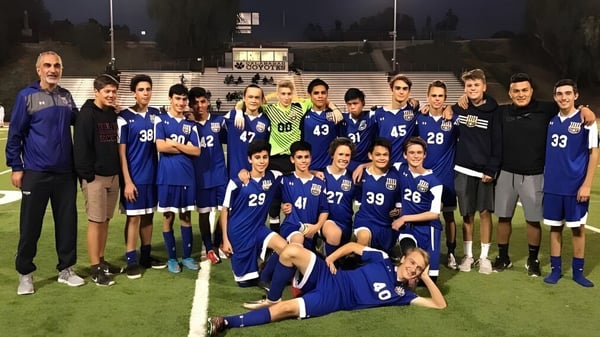 Un grupo de estudiantes de la Calabasas High School posan juntos de noche en un campo de fútbol con marcador y luces del estadio.