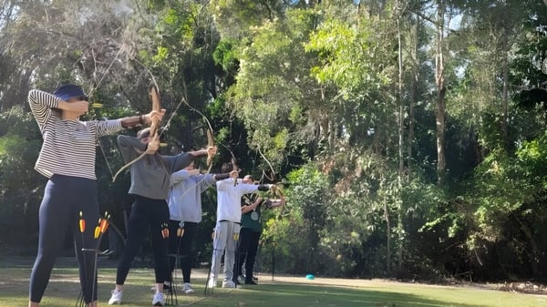Estudiantes del Calamvale Community College practican tiro con arco al aire libre en medio de un entorno verde.