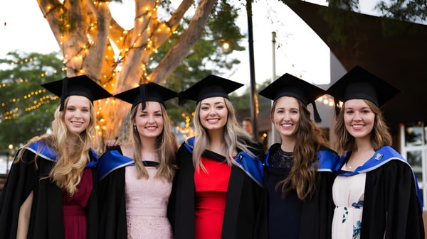Cinco estudiantes están juntas en sus togas de graduación frente a un árbol en el campus del Calamvale Community College.