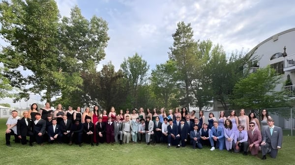 Un gran grupo de estudiantes de Calgary Christian School se reúne al aire libre frente a un edificio con árboles de fondo.