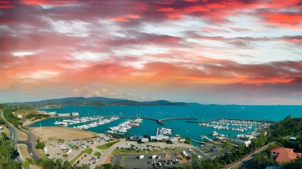 Toma aérea de un puerto costero con montañas al fondo al atardecer cerca del Caloundra Christian College.