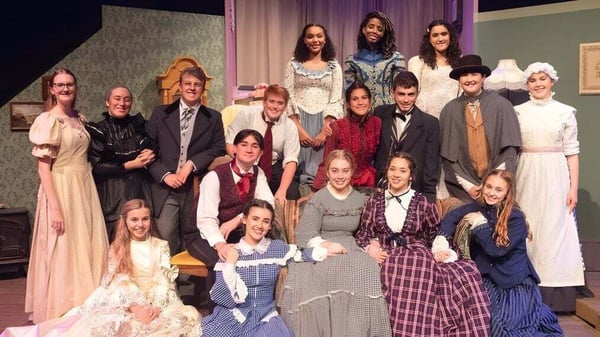 Estudiantes de la Calvary Christian Academy posan juntos en trajes históricos en un escenario con cortina y decorado.