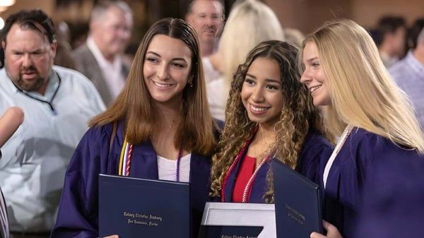 Tres estudiantes en ropa de graduación sostienen orgullosamente sus diplomas en la ceremonia de graduación de la Calvary Christian Academy.