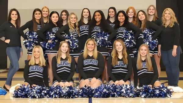 Un grupo de animadoras de la Calvary Day School posan con uniformes uniformes frente a un fondo neutral.