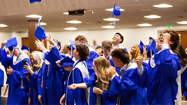 Un grupo de graduados en togas azules celebra su graduación en el interior decorado de la Calvary Day School.