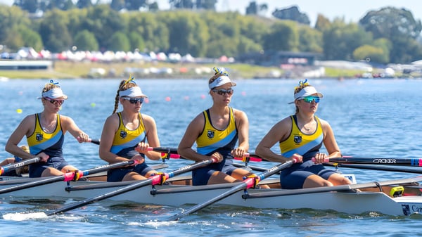 Cuatro remeras en el agua frente a un fondo de árboles y edificios en el campus de la Cambridge High School.