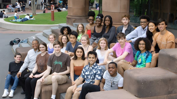 Un grupo de estudiantes de la Cambridge Rindge and Latin High School se reúne en el área exterior con edificios y áreas verdes de fondo.