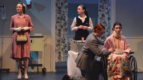Cuatro estudiantes de la Camden Hills Regional High School representan una escena de teatro con trajes históricos en una sala con cortinas florales.