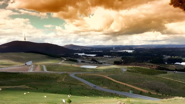 Paisaje con colinas y una ciudad al fondo bajo un cielo nublado cerca del Canberra College.